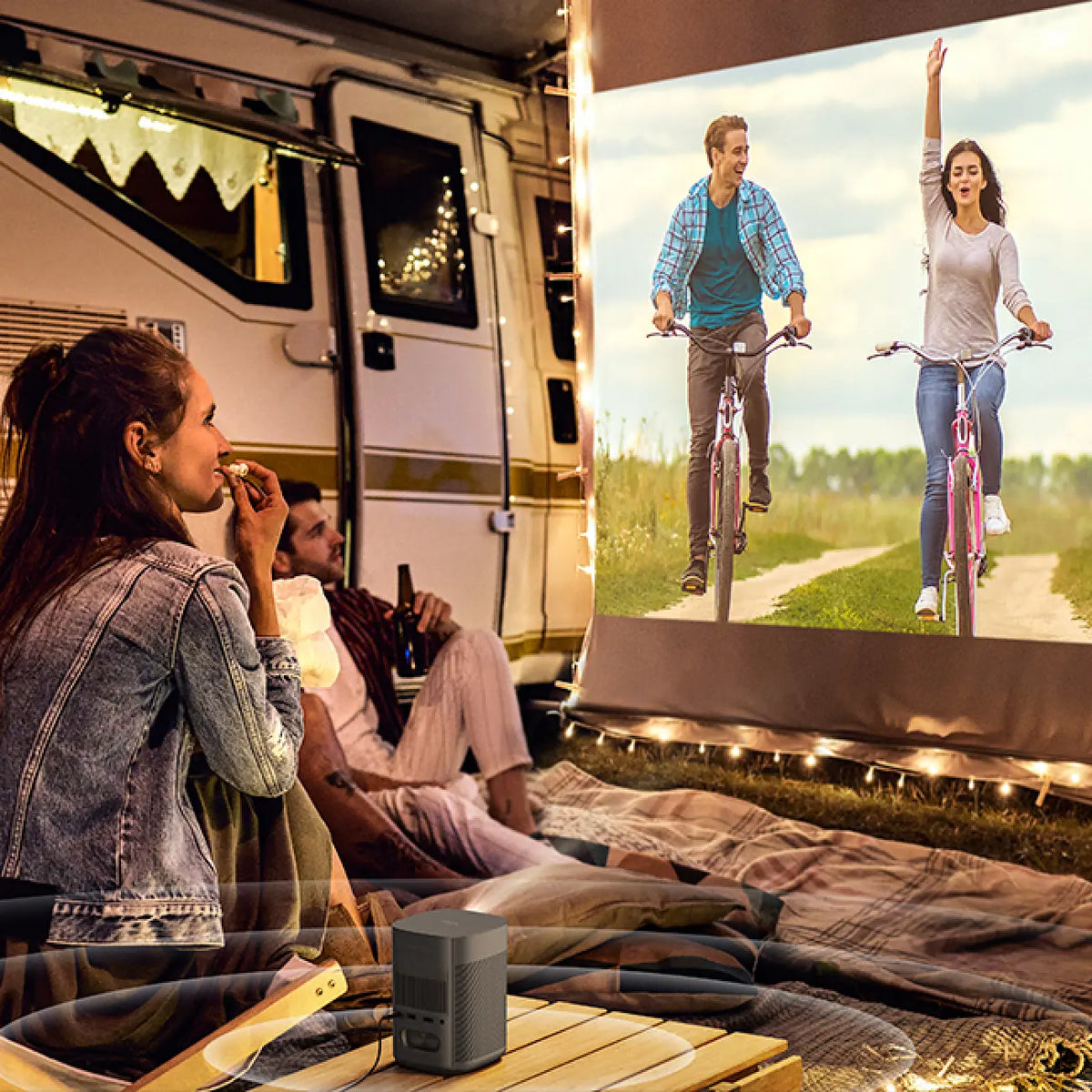 A couple enjoying an outdoor movie night next to their camper van using a portable projector.