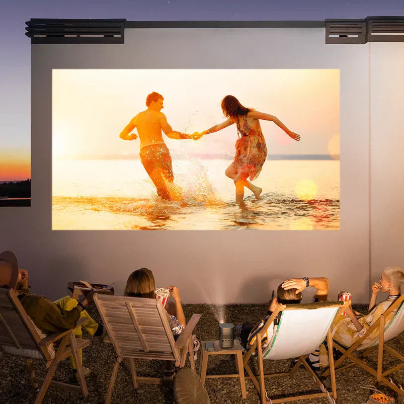 Friends watch a movie projected on an outdoor wall at dusk. An XGIMI projector is positioned on a small wooden table