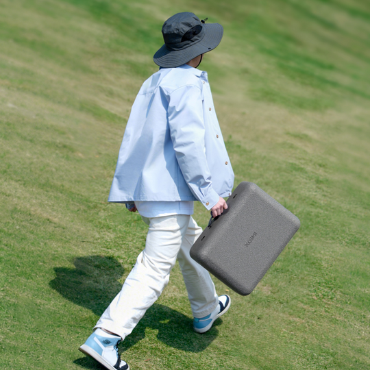 Person carrying MoGo 4 Laser Outdoor Collection portable projector case on grassy hill.